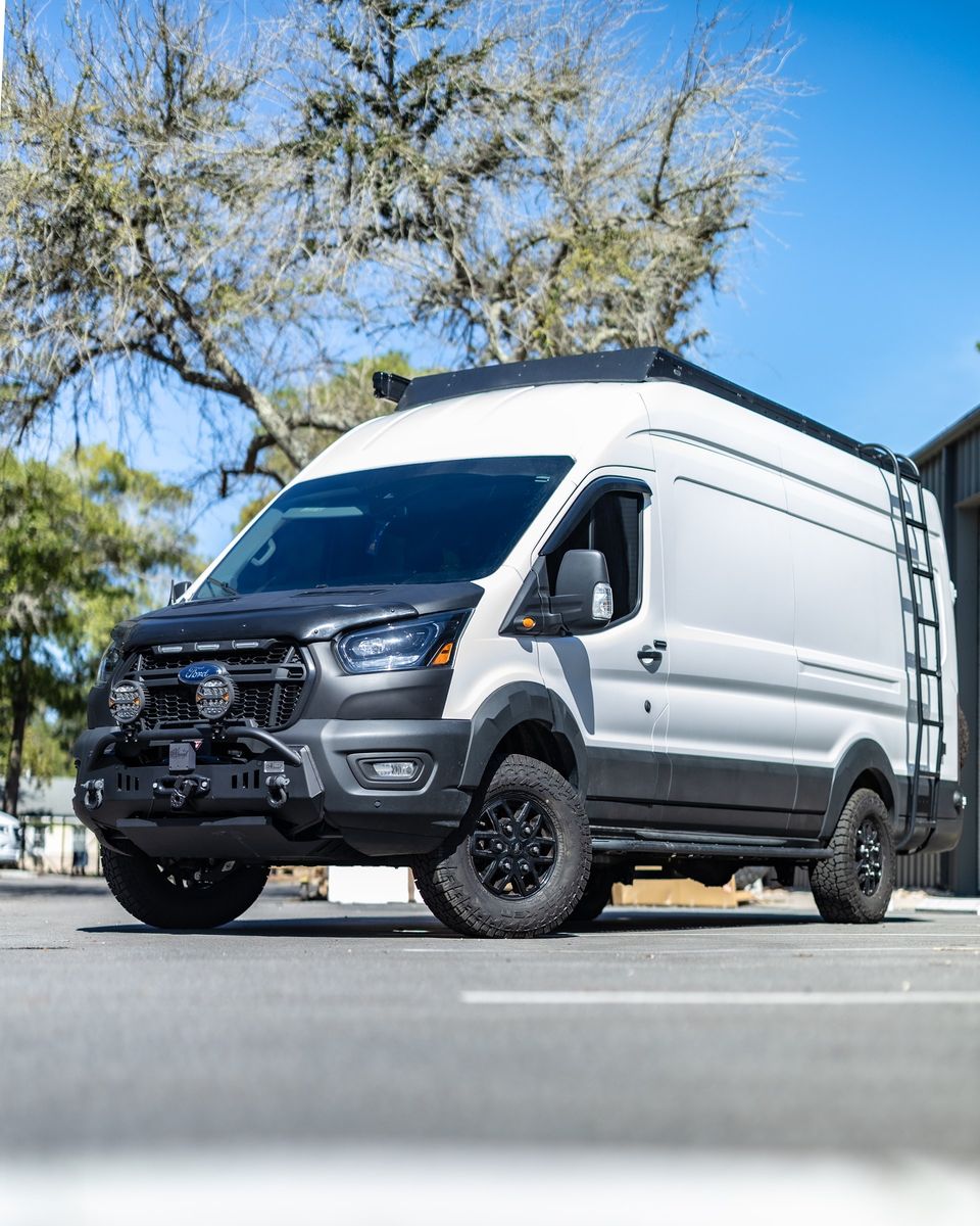 A white Ford Transit camper with a roof rack and ladder
