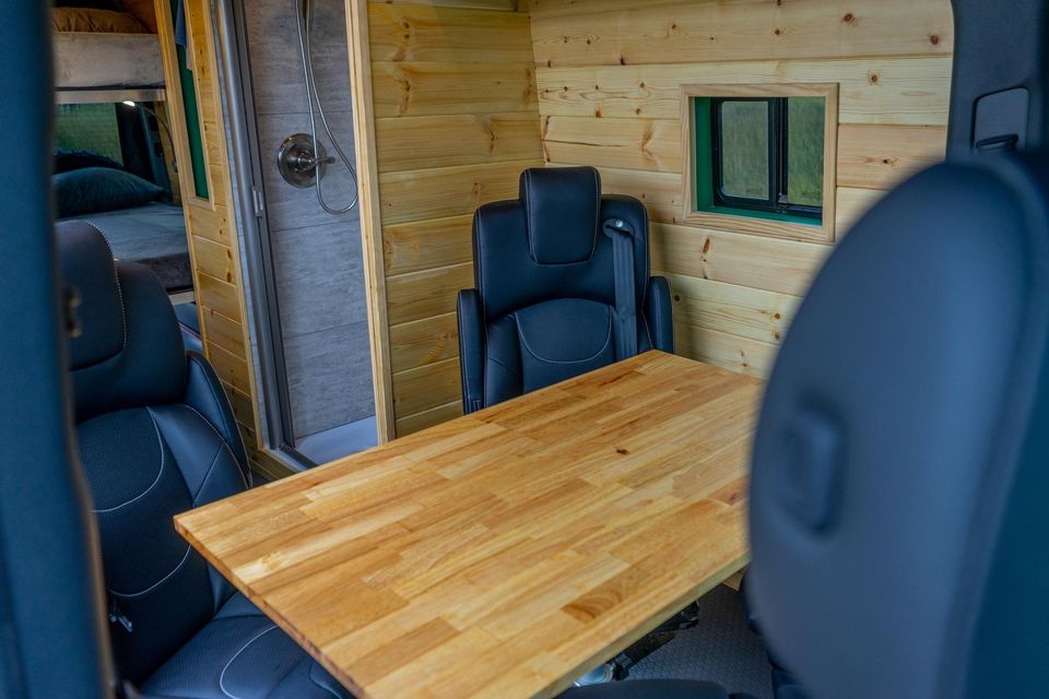 Leather captain chairs around a wood table inside a custom van
