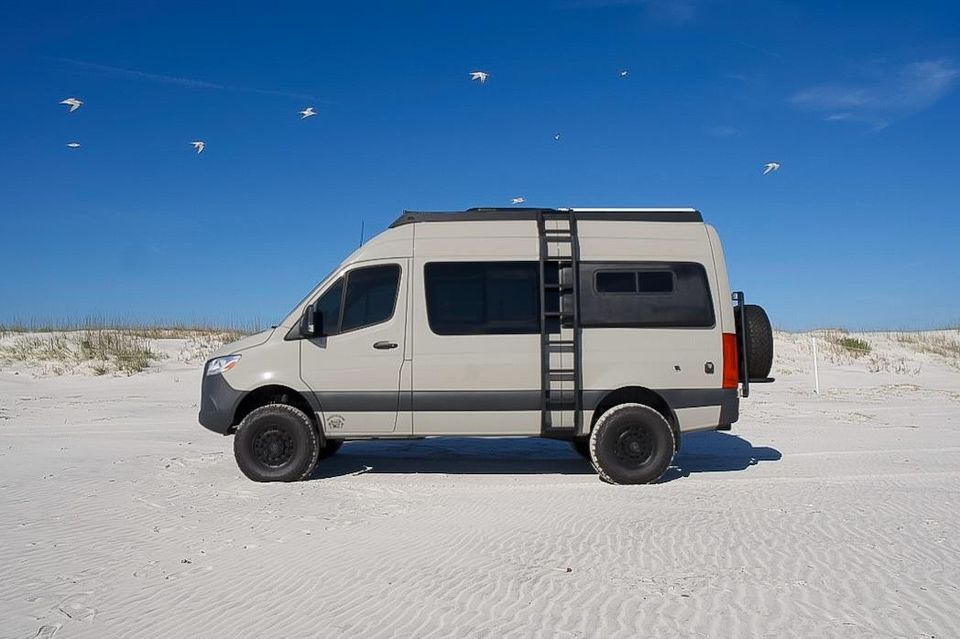 A sand-colored Sprinter camper van on the beach