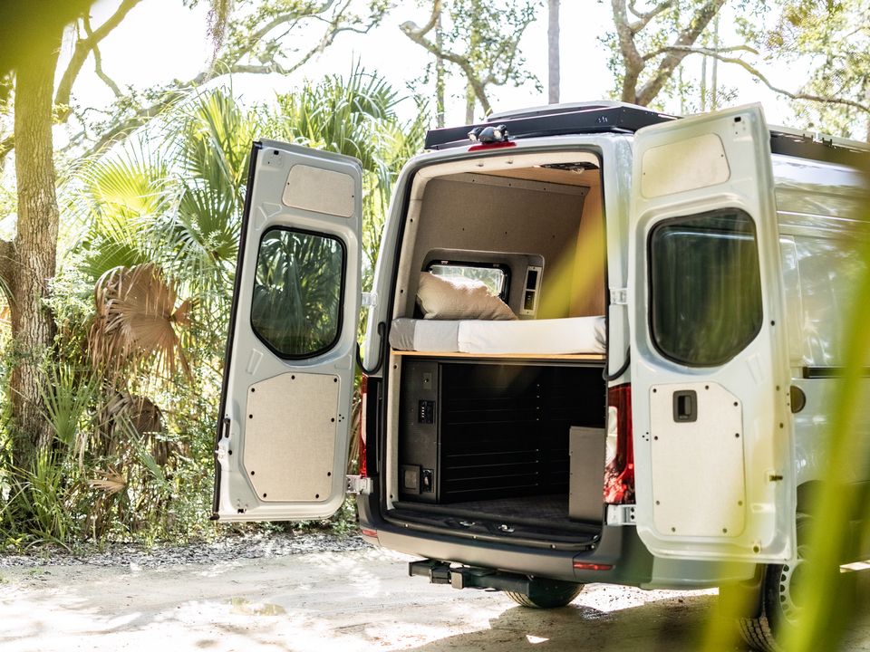 A Sprinter with the rear doors open to the gear garage, among palms