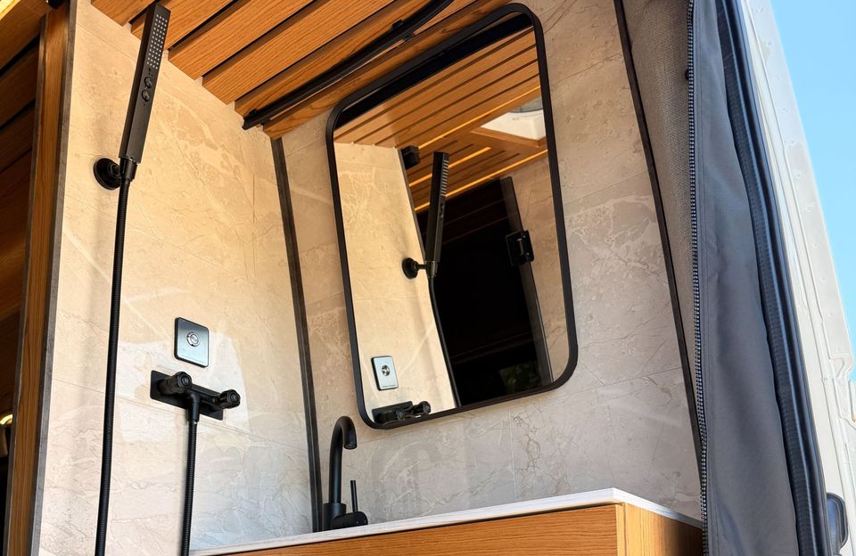 A van shower with a wood slat ceiling, a black framed mirror and black fixtures