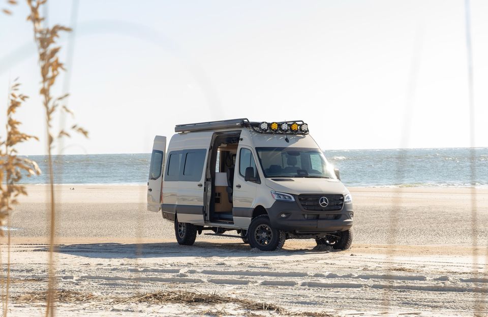 A Sprinter camper van parked on a beach with its sliding door open