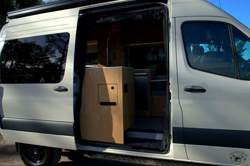 A Sprinter camper van with the sliding door open to a wood cabinet