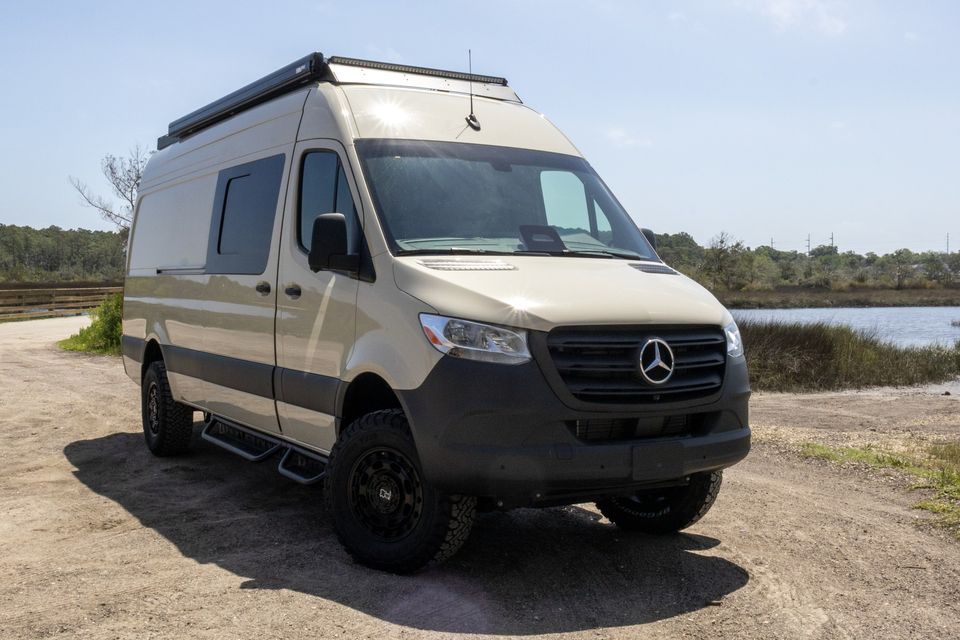 A sand-colored Sprinter 170 camper van by the marsh
